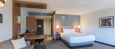 Ein Hotelzimmer mit Bett, Schreibtisch, Stuhl, Sofa und Badezimmer.