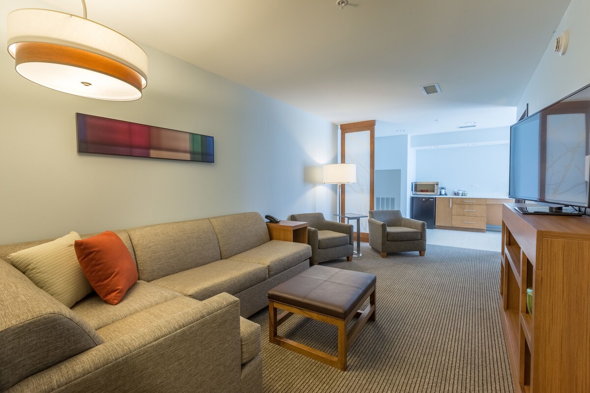 A modern living room with a sofa, armchairs, a coffee table, a TV, and a painting on the wall.