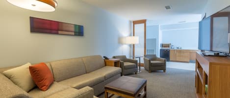 A modern living room with a sofa, armchairs, a coffee table, a TV, and a painting on the wall.