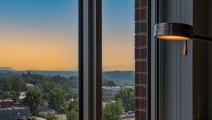 Une vue depuis une fenêtre, avec un luminaire suspendu, donnant sur un paysage urbain composé d’immeubles et de verdure.