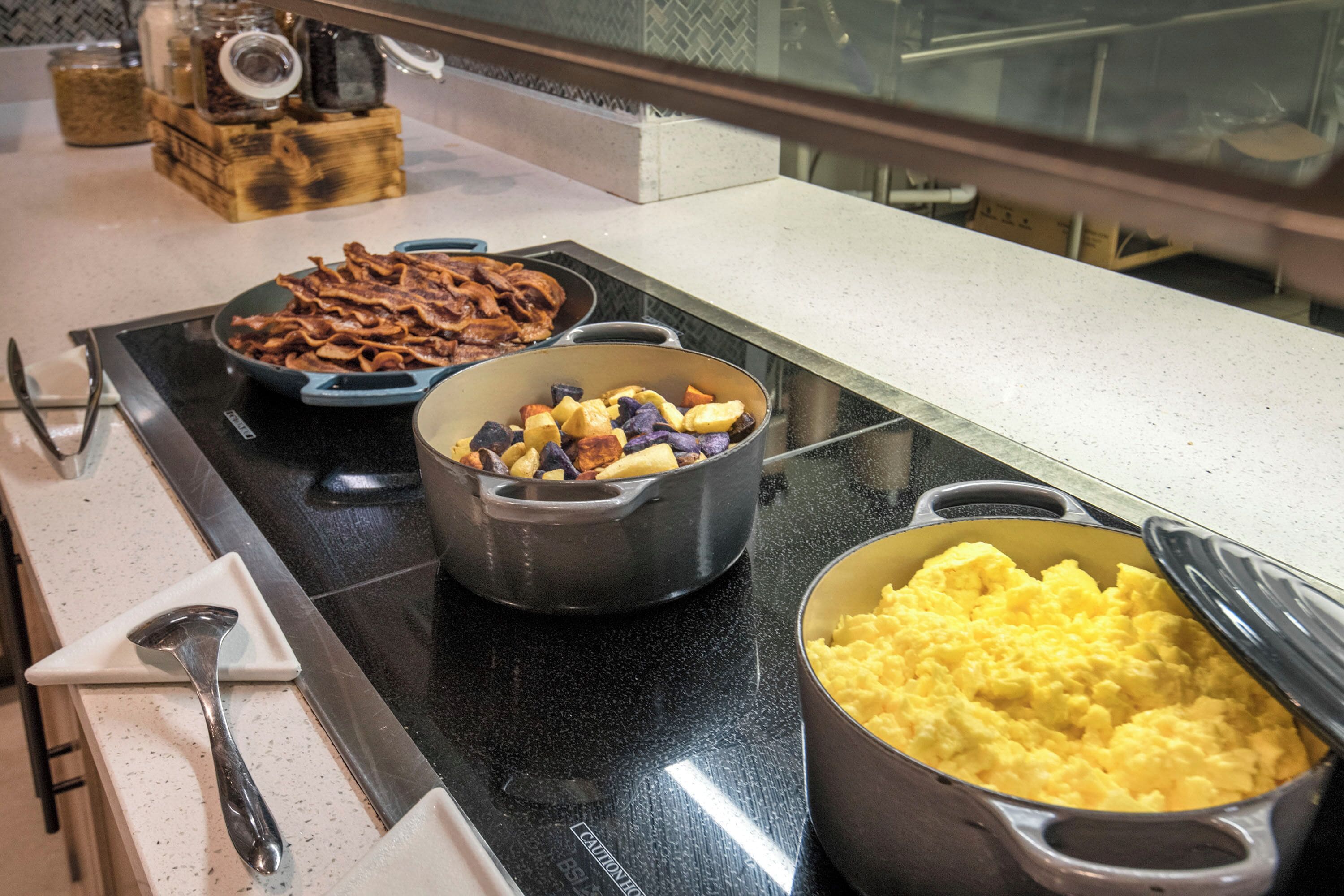 Una encimera de cocina con varios platos, incluyendo lo que parecen huevos revueltos, un cazo y un plato con carne y verduras.