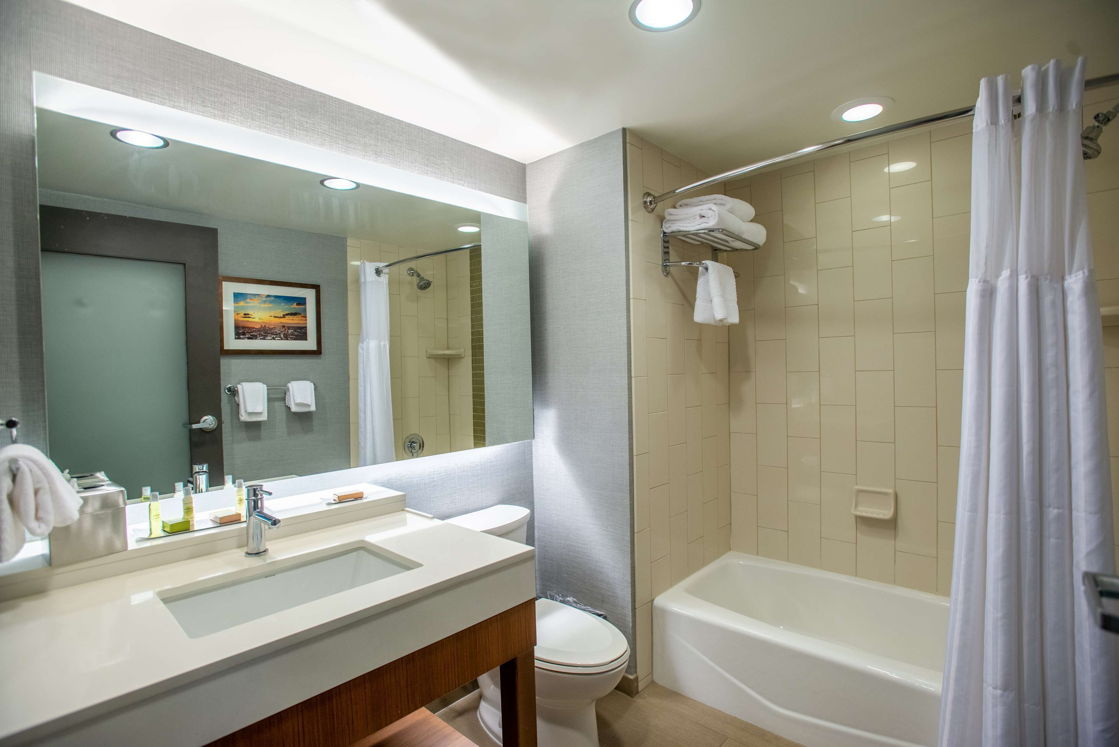 A modern bathroom with a large mirror, a sink, a toilet, and a bathtub.