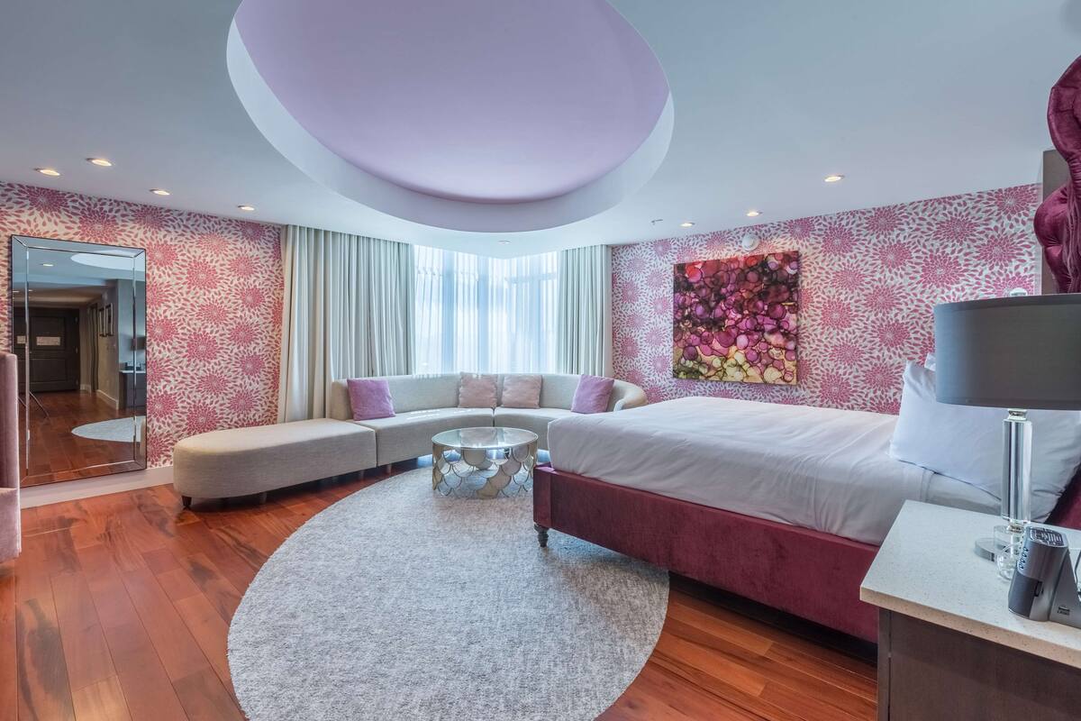 Ein modernes Schlafzimmer mit einem großen Bett, einem Sofa, einem runden Couchtisch und einem großen Spiegel.