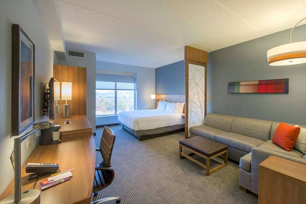 Ein Hotelzimmer mit einem Bett, einer Couch, einem Schreibtisch mit Stuhl, einer Lampe und einem Fenster.