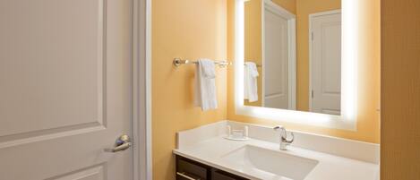A bathroom with a white sink, dark cabinets, and a mirror with lights.