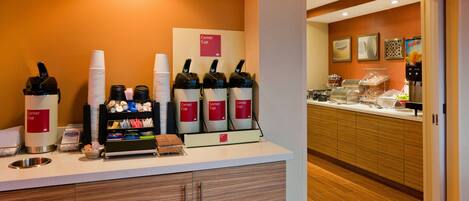 A hotel reception area with a coffee station, a counter with stacked cups, and a refrigerator.