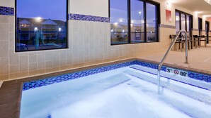 Zona de jacuzzi con paredes de azulejos y ventanas con vista a un estacionamiento.