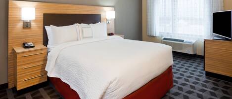 A hotel room with a large bed, bedside tables, a TV, and a window with curtains.