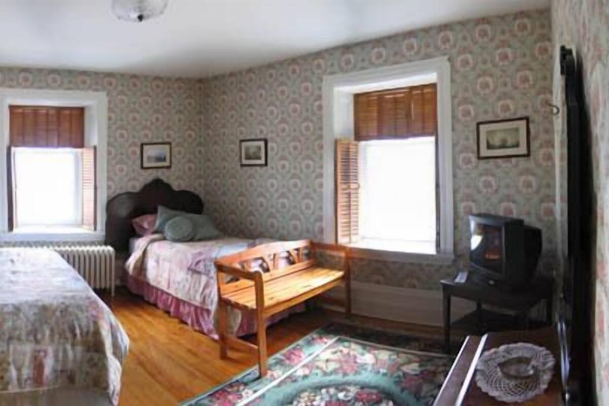 A bedroom with two beds, a wooden bench, a radiator, and a television.