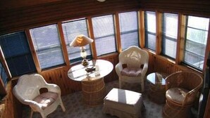 Interior acogedor de una cabaña con una mesa redonda, dos sillas de mimbre, un banco acolchado y un taburete pequeño.