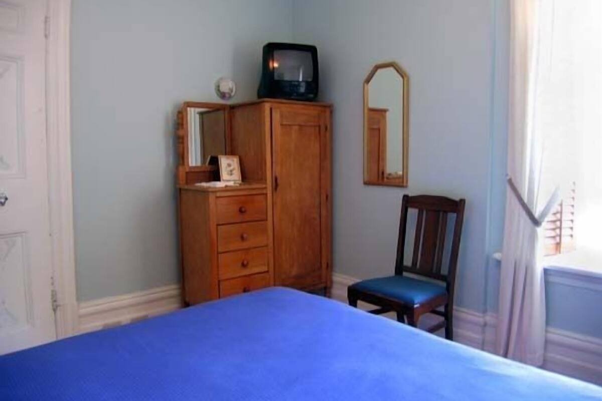 A bedroom with a bed, a wooden dresser, a chair, a television, and a mirror.