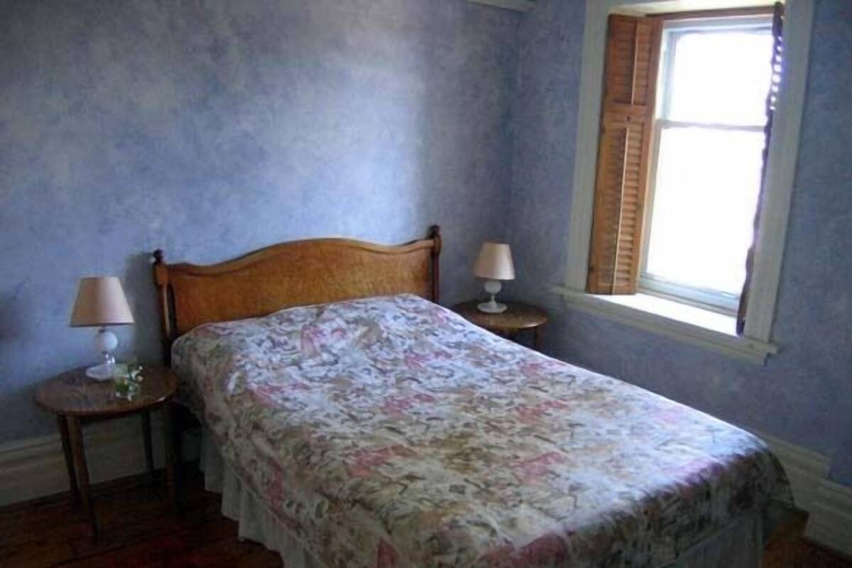 A bedroom with a wooden bed, two bedside tables with lamps, a window with shutters, and a floral bedspread.