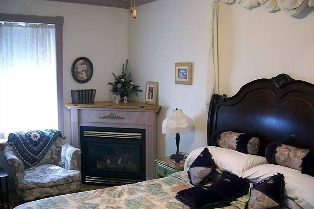 A bedroom with a bed, a chair, a fireplace, and a nightstand.