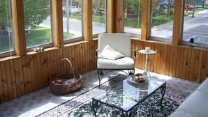 Una habitación acogedora con un ventanal grande, una silla blanca, una mesa de centro de vidrio y una alfombra estampada.