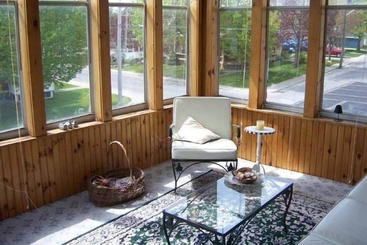 A cozy room with a large window, a white chair, a glass coffee table, and a patterned rug.