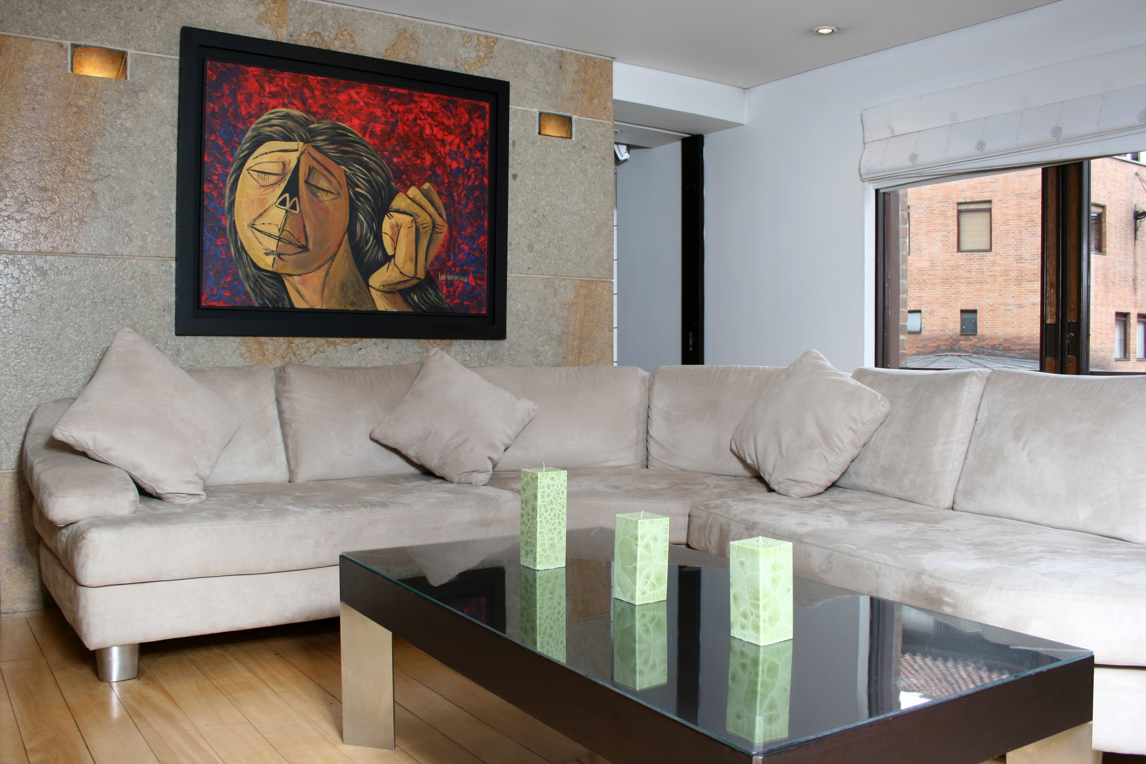 A modern living room with a beige sectional sofa, a glass coffee table, and a framed artwork on the wall.