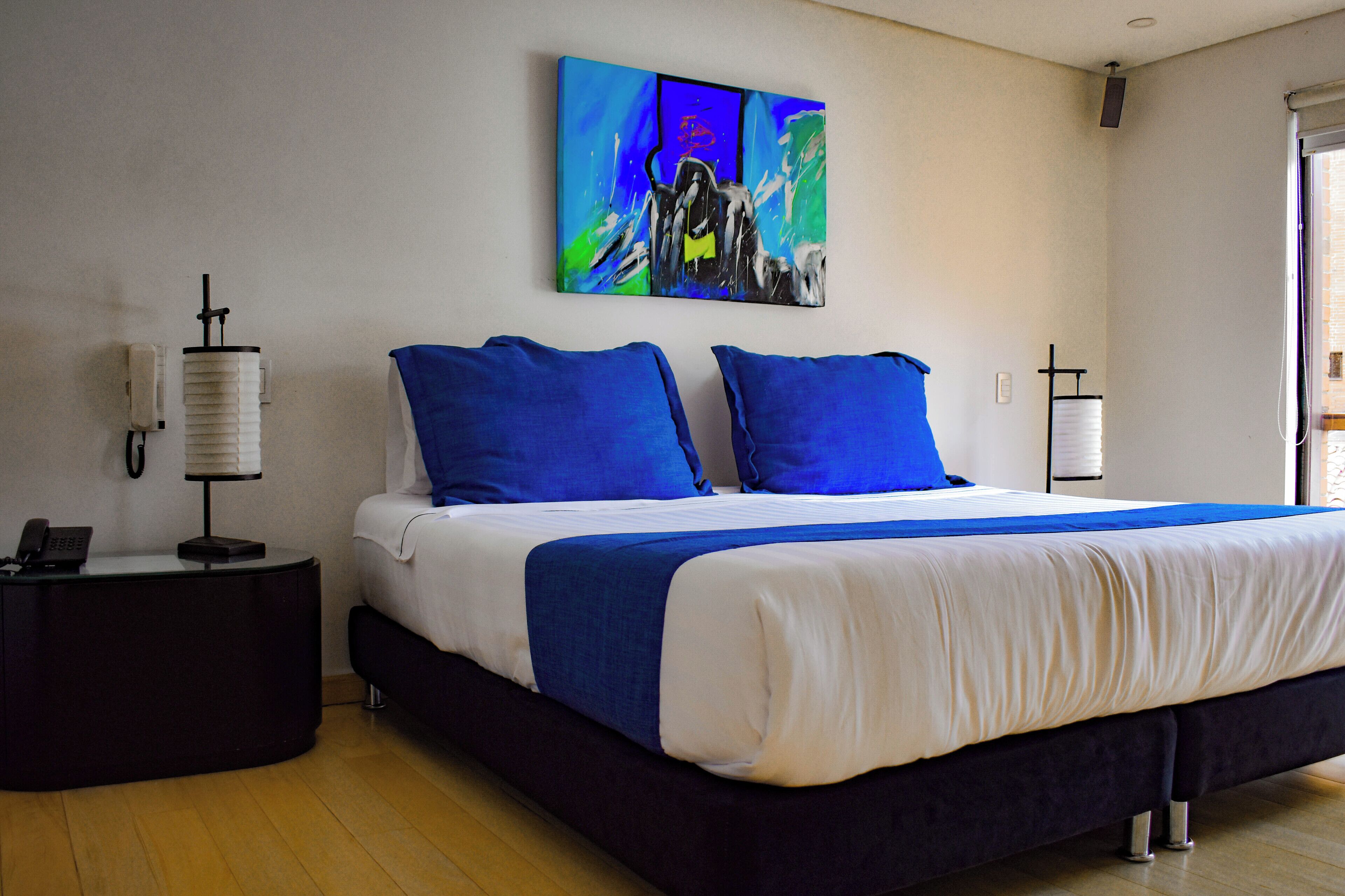 Une chambre à coucher moderne avec un grand lit, des oreillers bleus et un tableau abstrait aux couleurs vives accroché au mur.