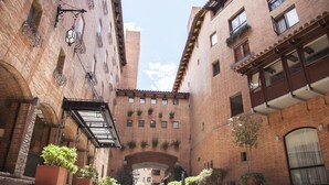 Un estrecho callejón con edificios de ladrillo, plantas en macetas y mesas al aire libre.