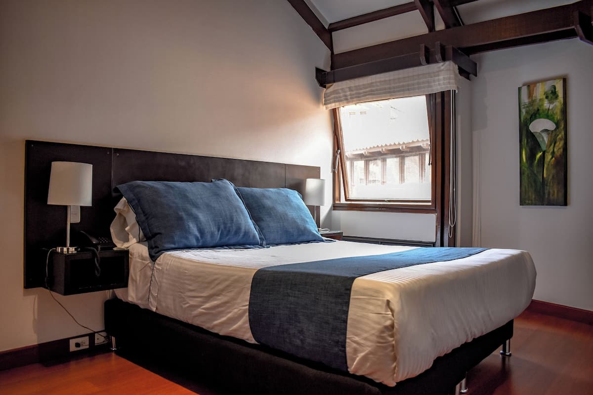 Een hotelkamer met een bed, nachtlampjes, een raam met uitzicht en een schilderij aan de muur.