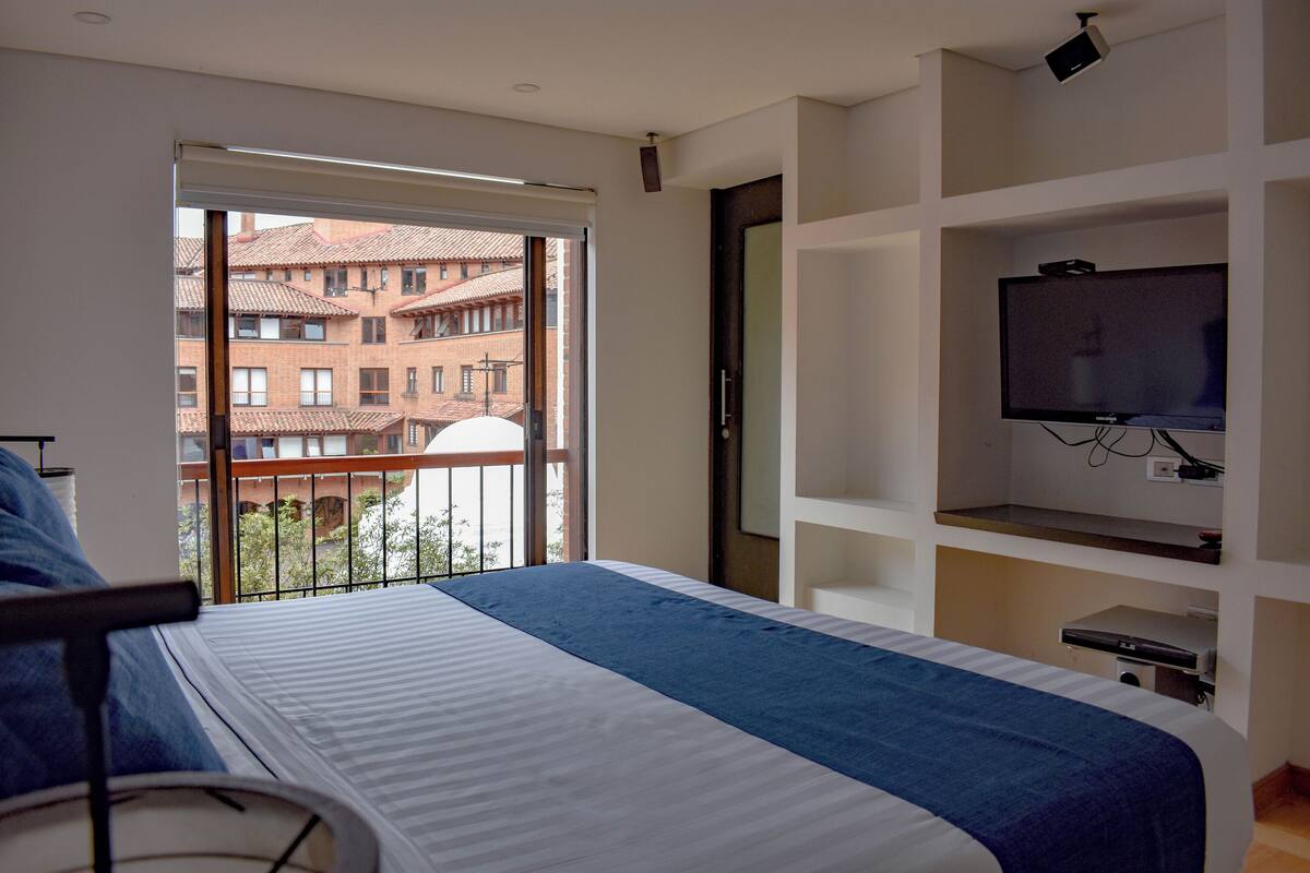 Een slaapkamer met een bed, een televisie en uitzicht op gebouwen door een raam.