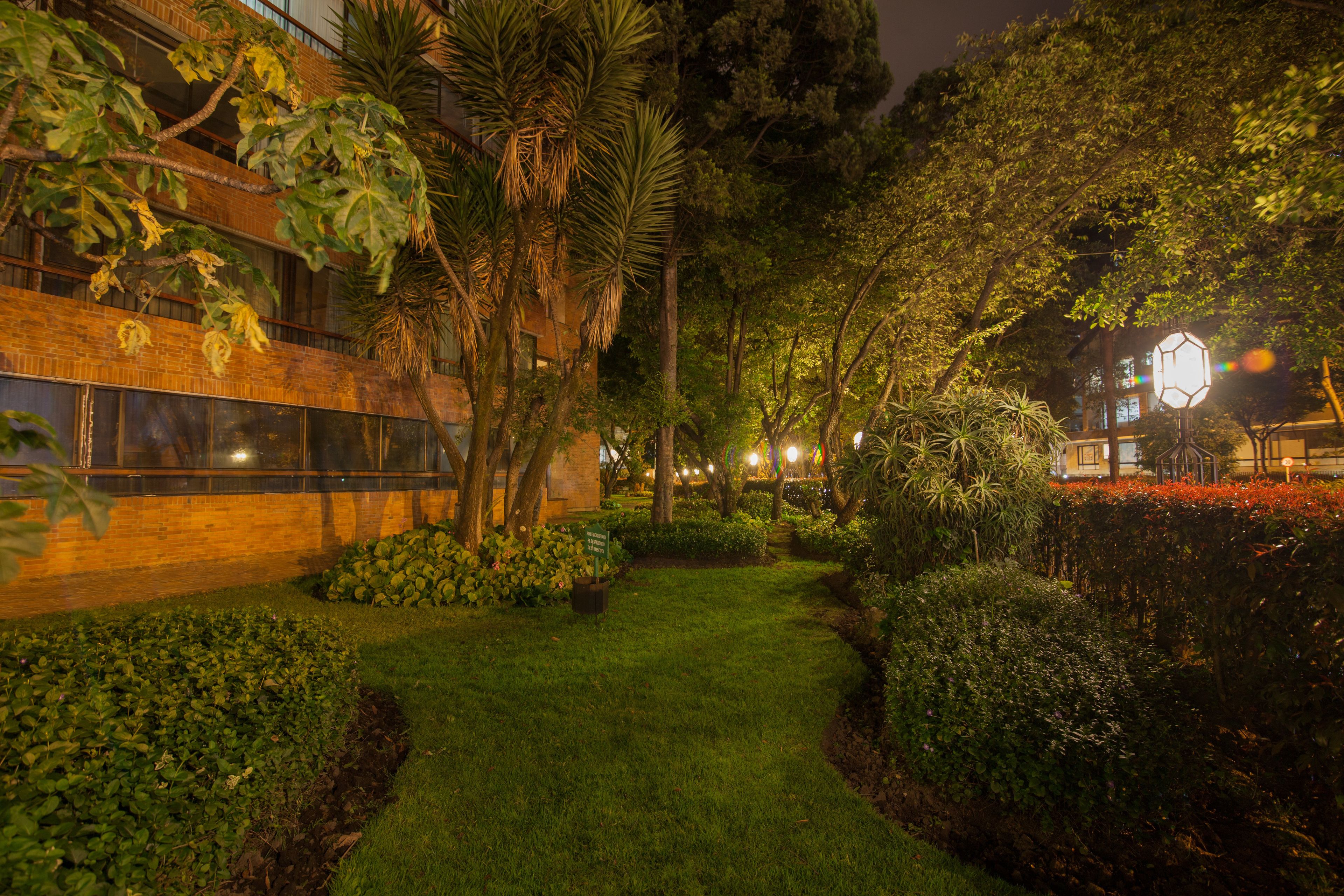 Un jardín cuidado con un sendero que lleva a un edificio de grandes ventanales y fachada de ladrillo.