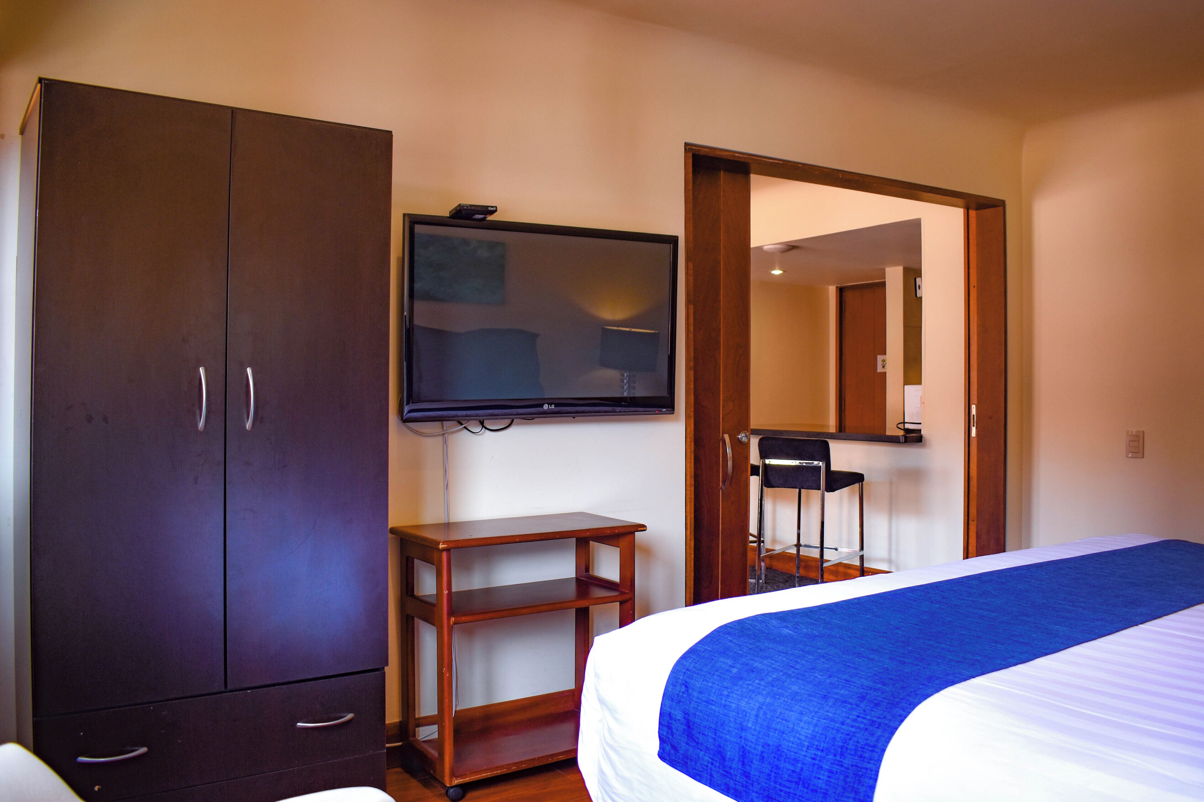 A hotel room with a bed, a wardrobe, a television mounted on the wall, and a desk with a chair.