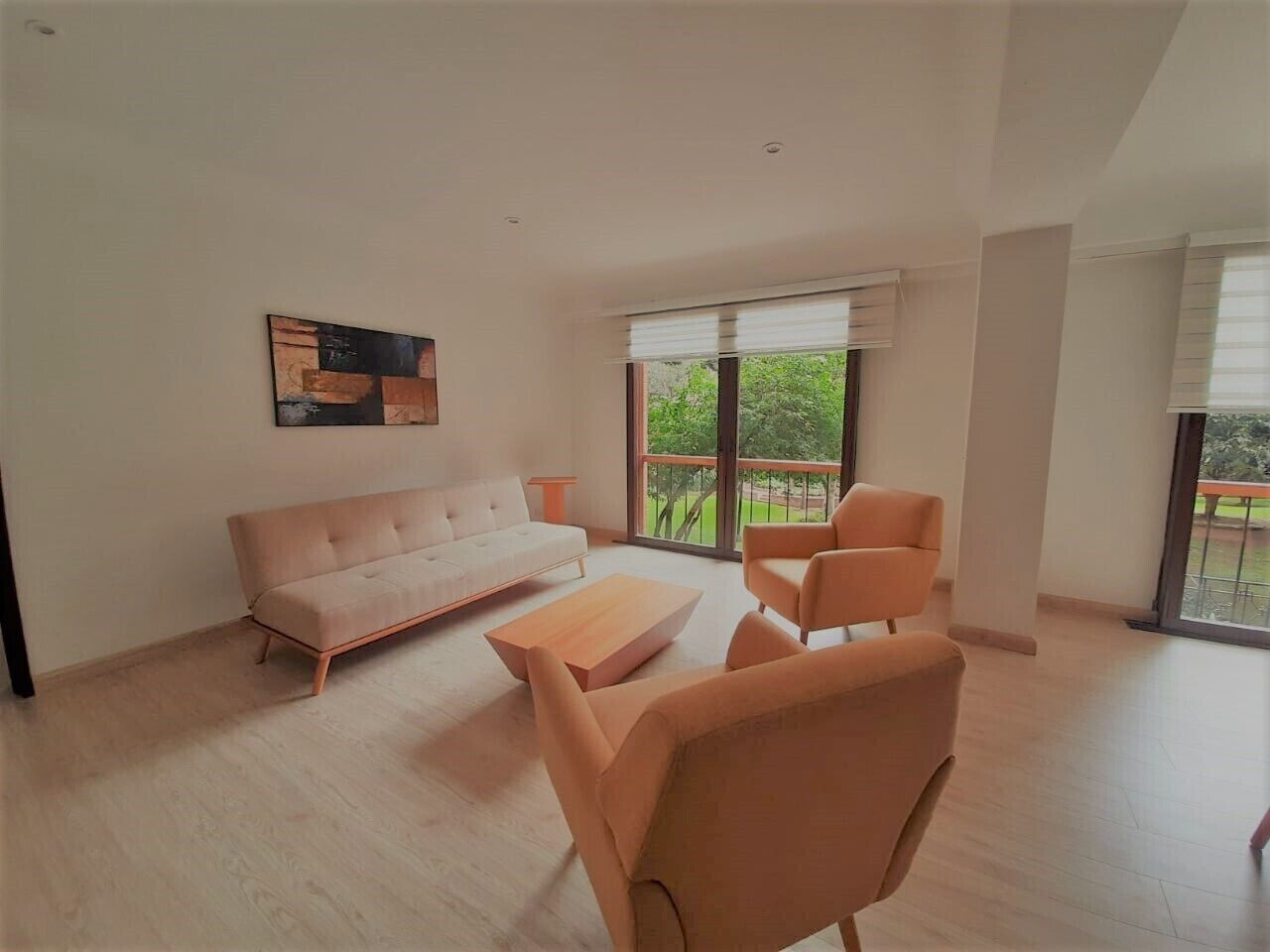 Ein geräumiges Wohnzimmer mit einem hellen Sofa, einem Couchtisch und einem Sessel. Ein großes Fenster bietet Blick auf die grüne Umgebung.