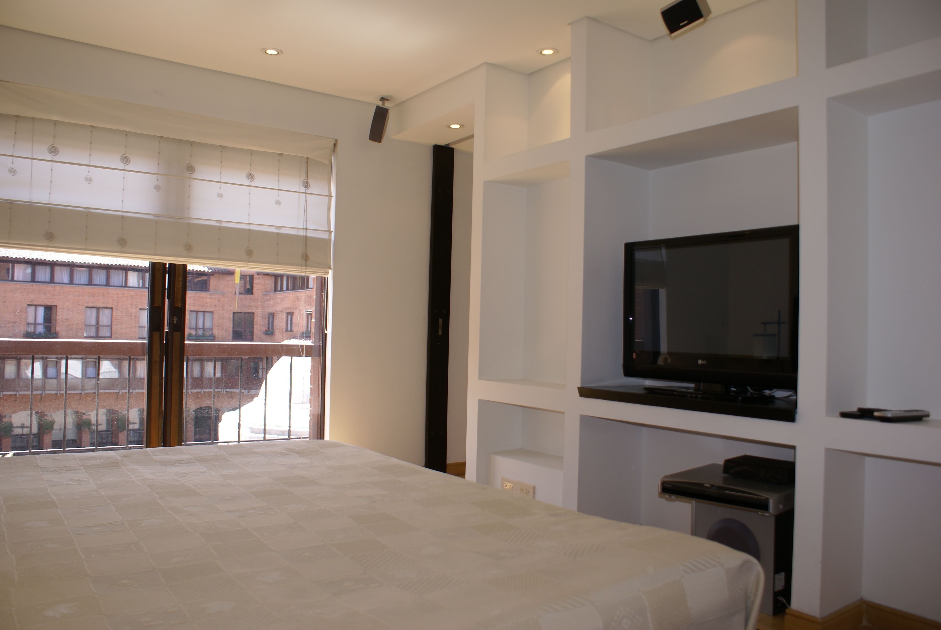 A bedroom with a large bed, a television on a stand, and a view of a building through a window.