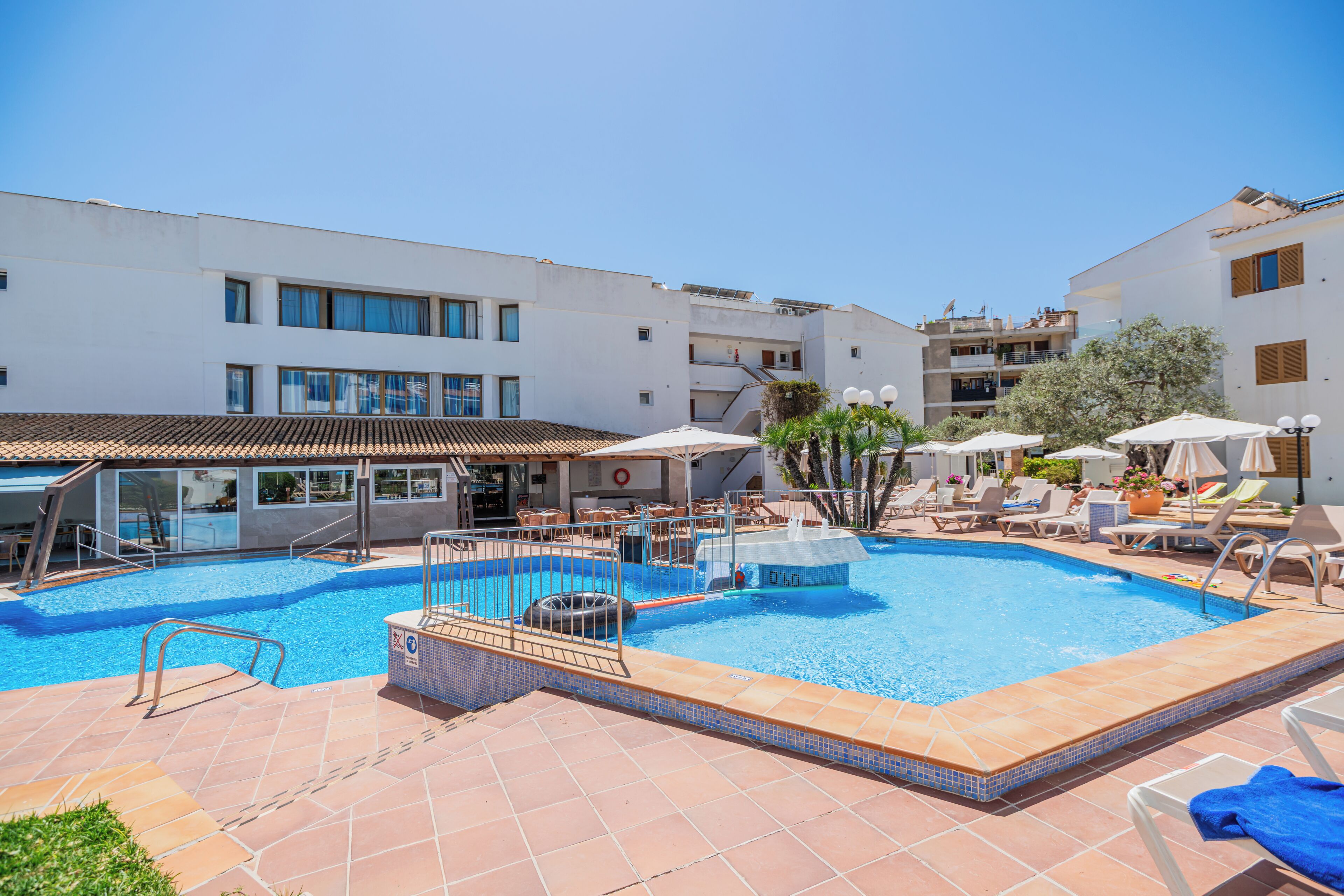 Una piscina amb gandules, un post de socorrista i un edifici amb balcons.