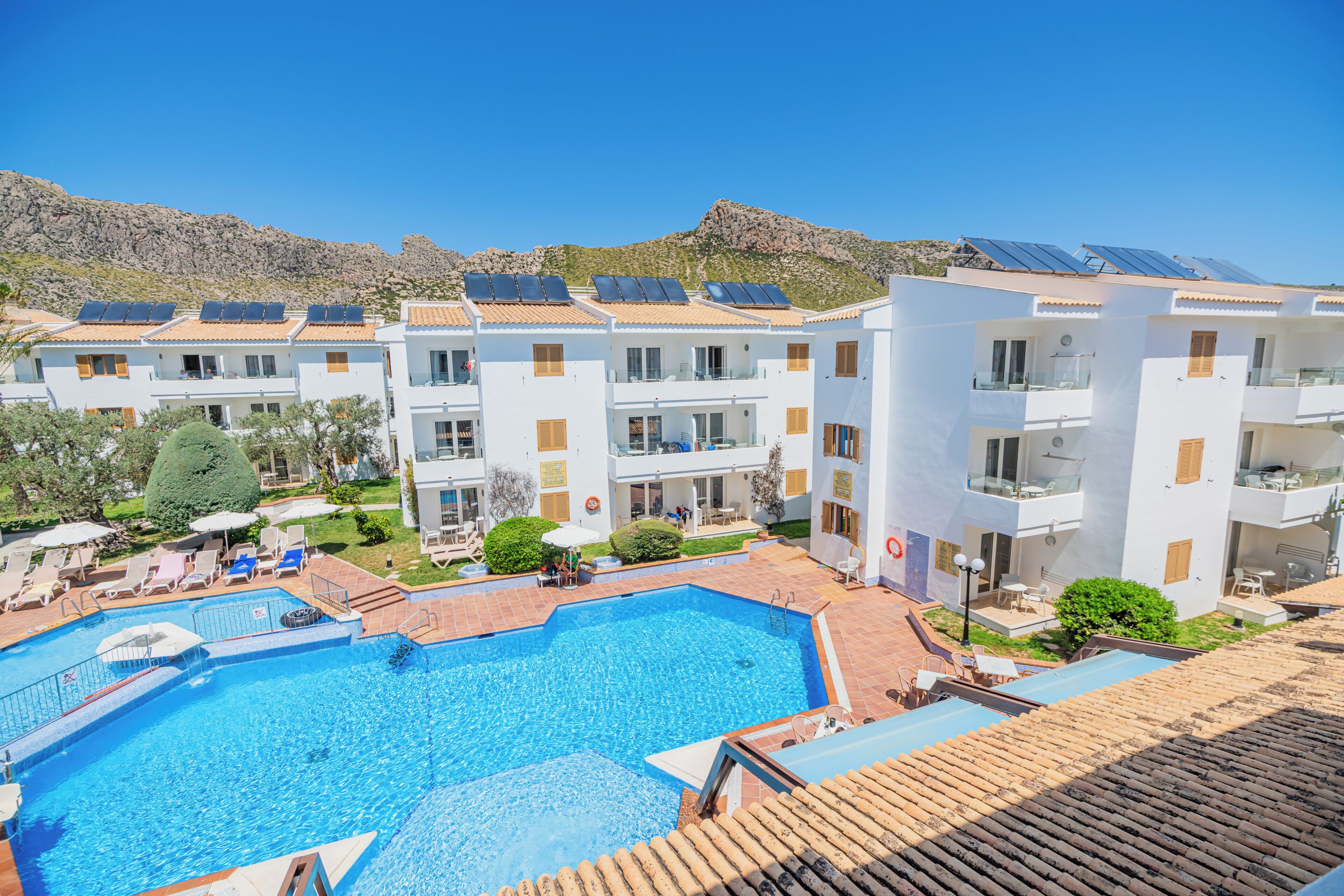 A hotel with a swimming pool, multiple balconies, and solar panels on the roofs.
