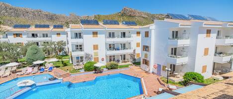 A hotel with a swimming pool, multiple balconies, and solar panels on the roofs.