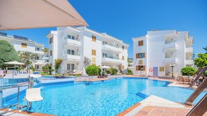 A swimming pool with a tiled deck, surrounded by white buildings with balconies.
