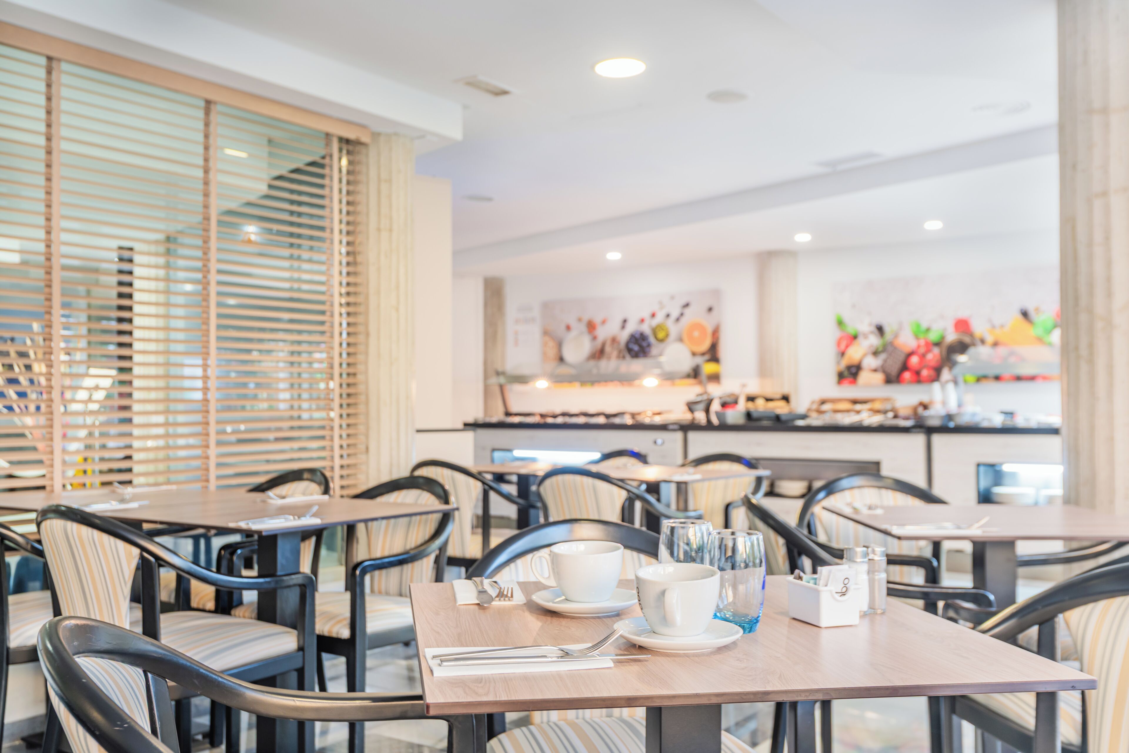 A restaurant with tables set for dining, chairs, and a buffet area in the background.