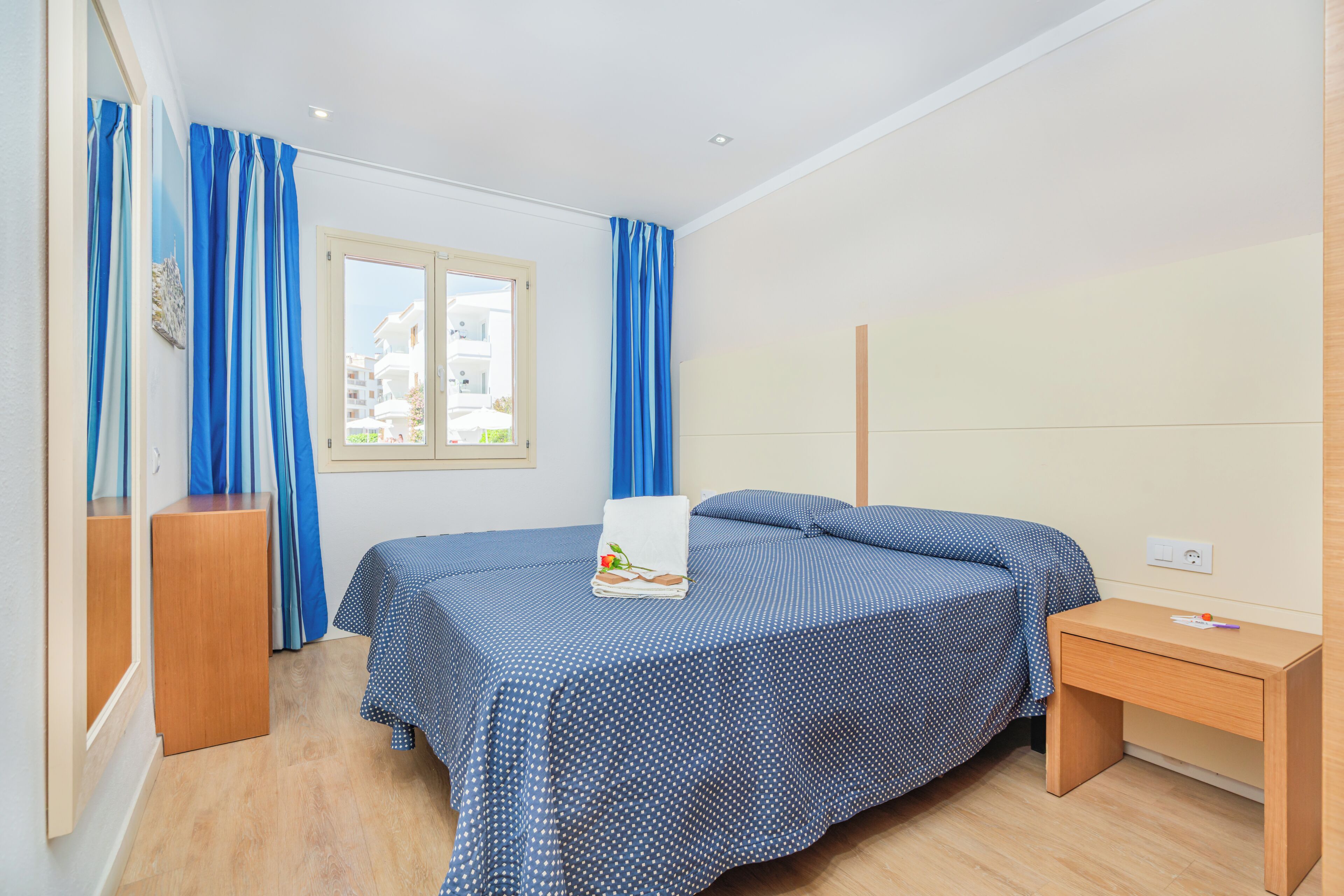 Un dormitorio con cama, mesita de noche, ventana y cortinas.