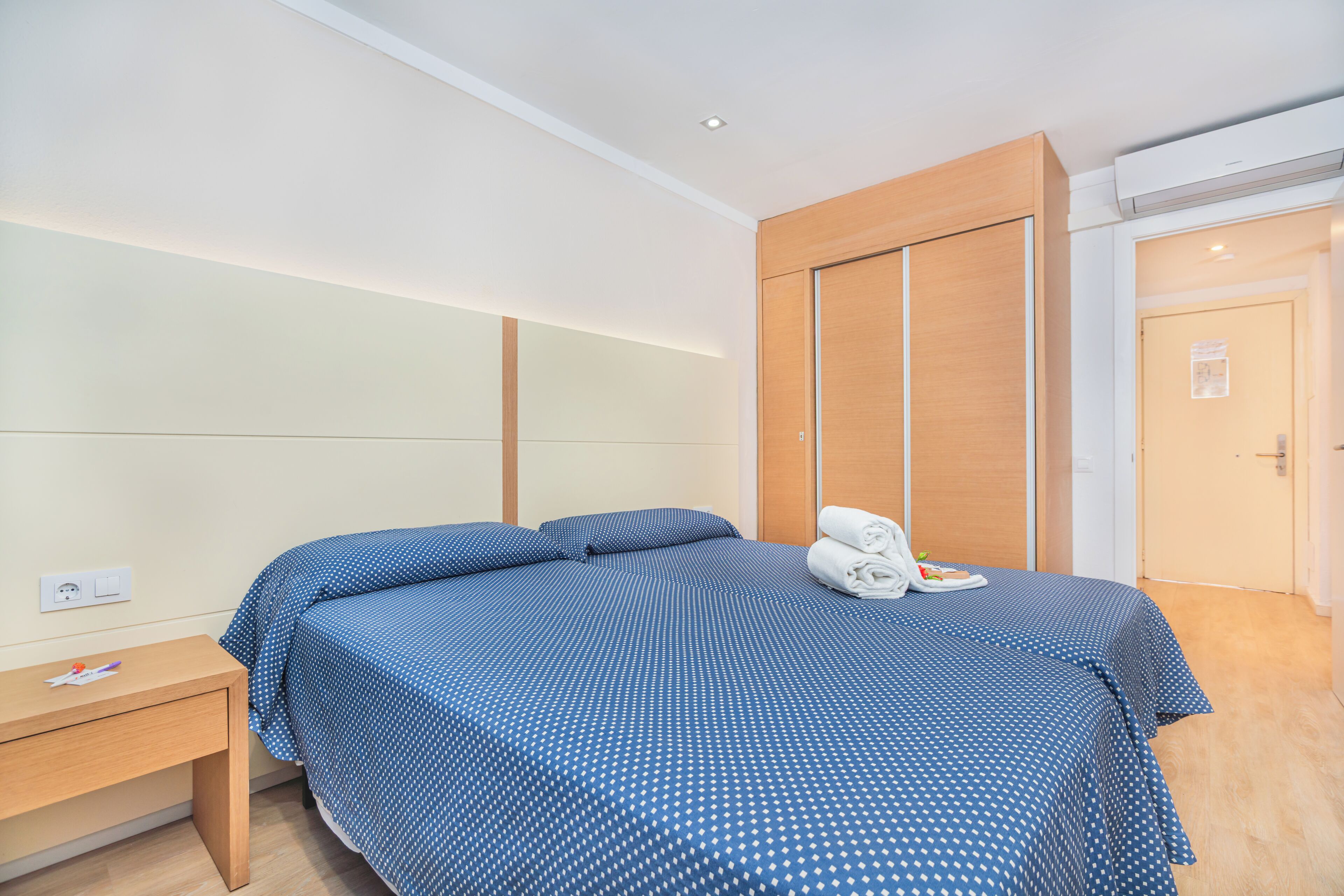 Un dormitorio con una cama, una mesita de noche, un armario de madera y una puerta.