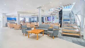 A spacious lobby with seating areas, a staircase, and a view of the sky.