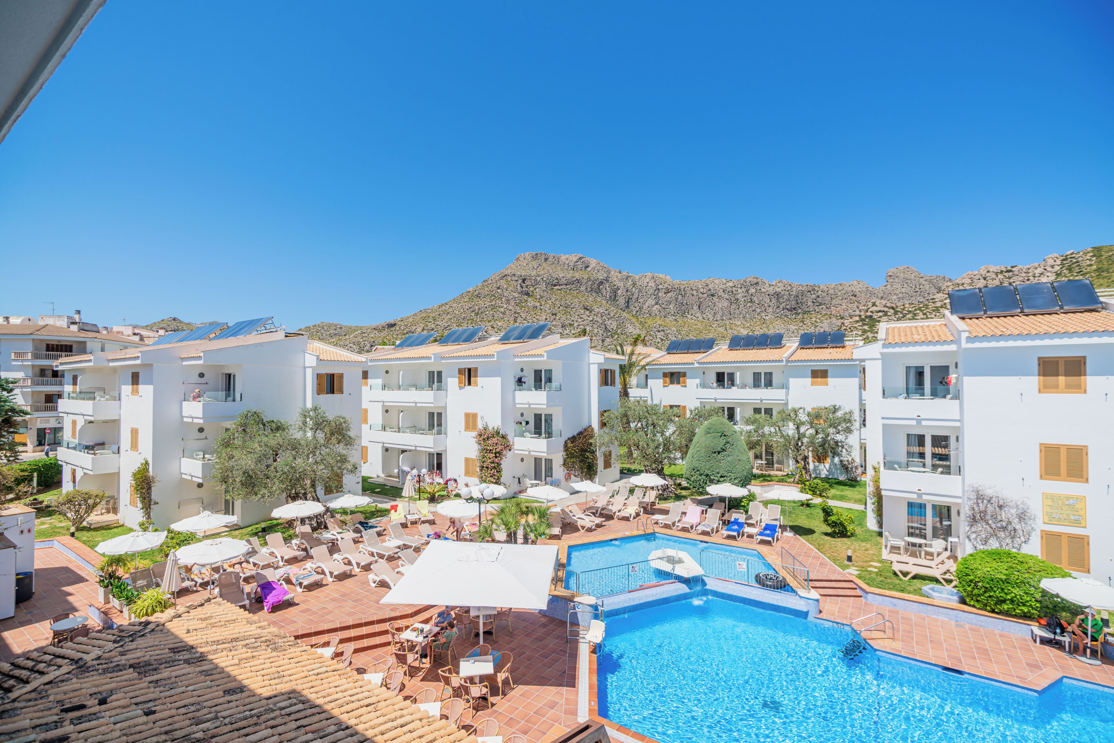 A hotel with a swimming pool, sun loungers, and solar panels on the roofs.