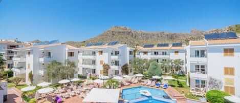 A hotel with a swimming pool, sun loungers, and solar panels on the roofs.
