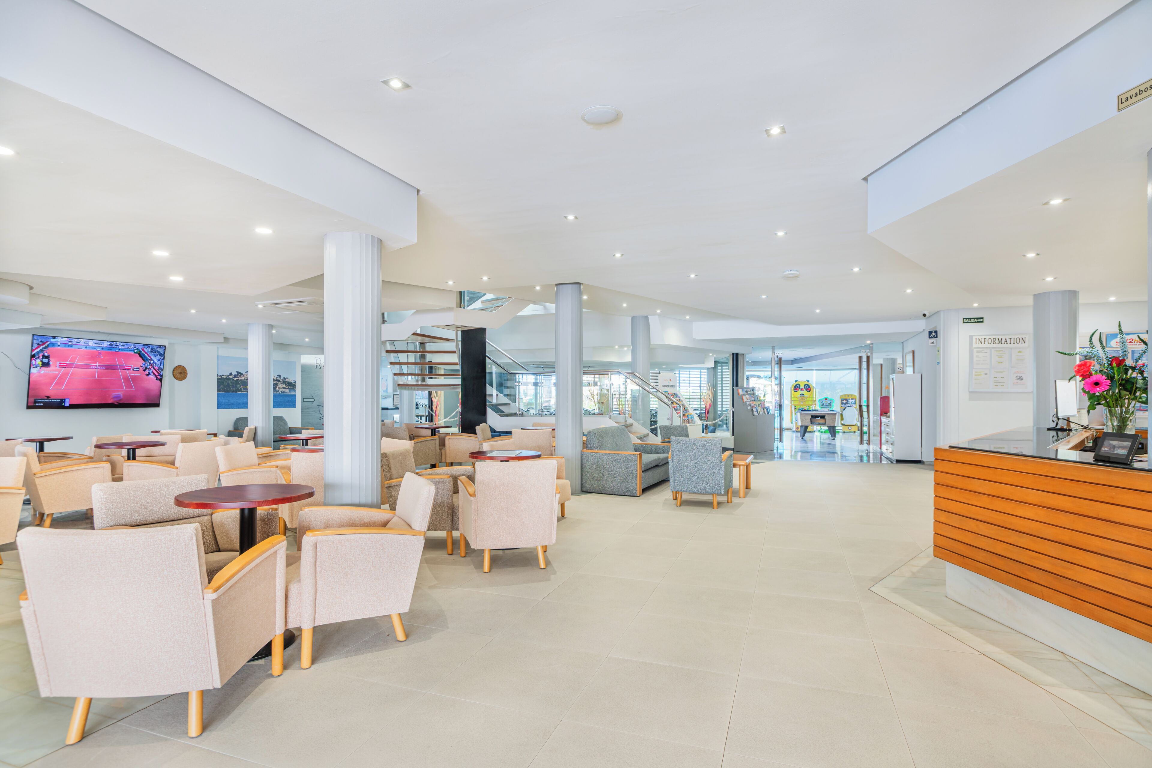 Un hall d’hôtel moderne, doté d’espaces aménagés avec des sièges, d’un comptoir d’accueil et d’un grand écran de télévision.
