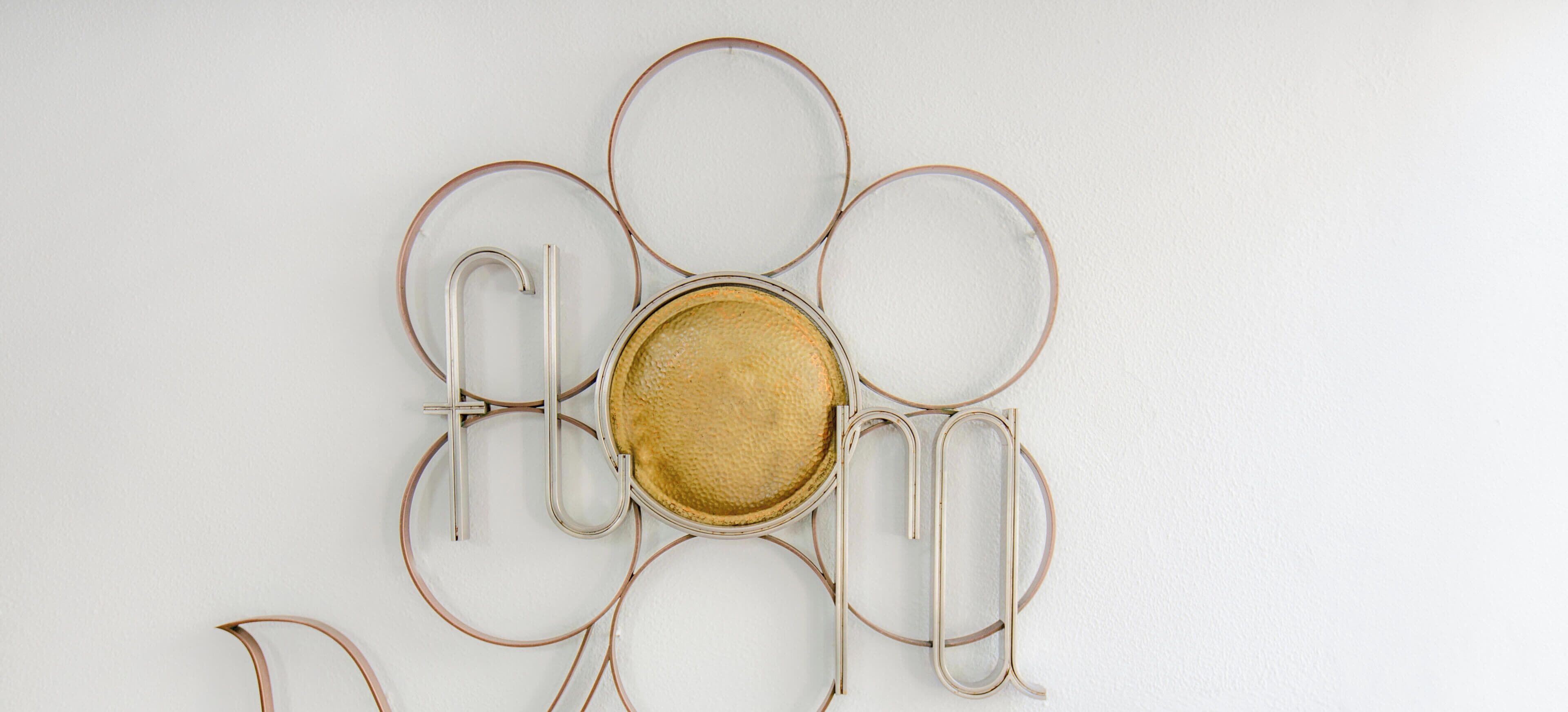 Eine an der Wand befestigte Metallskulptur mit kreisförmigen und geschwungenen Elementen.