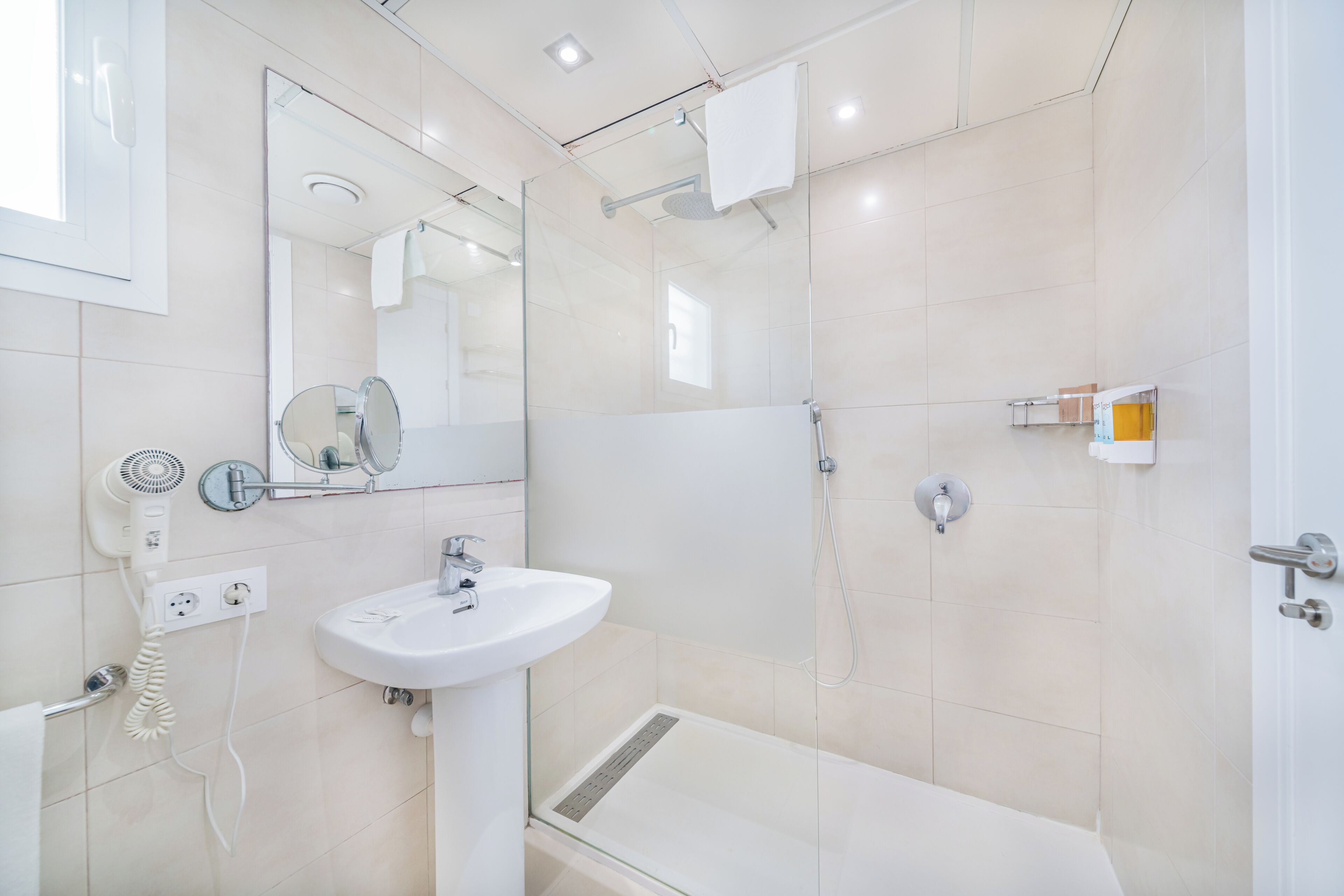 Un baño moderno con cabina de ducha de vidrio, un lavabo blanco y un secador de pelo de mano.