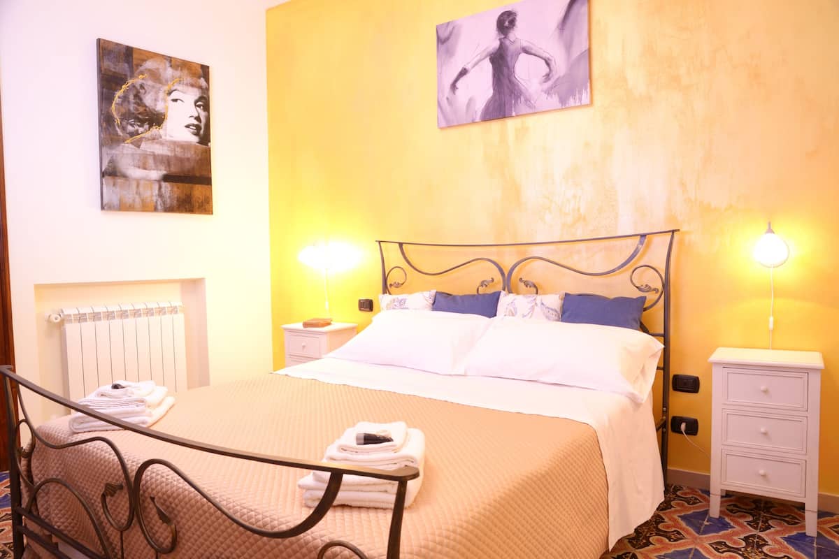 A hotel room with a bed, bedside tables, a radiator, and artwork on the walls.