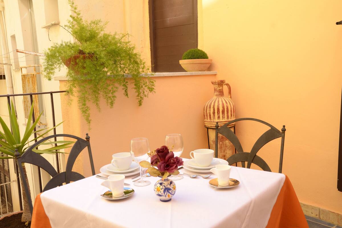 A table set for a meal with a vase of flowers, a potted plant, and a decorative pitcher.
