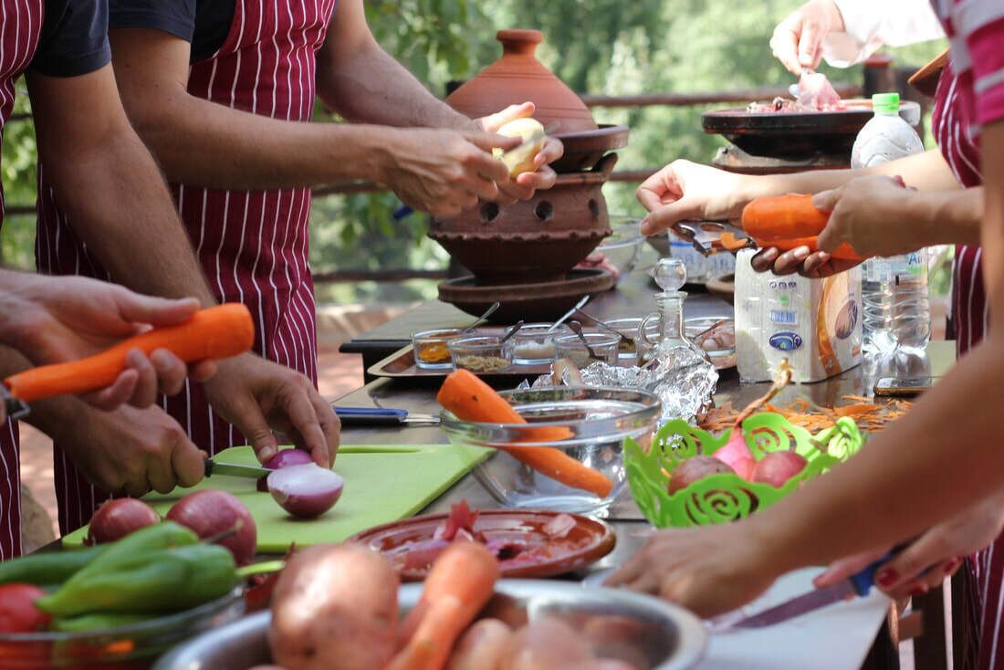 Eine Gruppe von Menschen bereitet im Freien Essen zu, mit Gemüse und Kochutensilien.