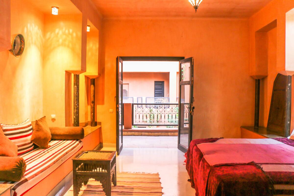 A room with a bed, a sofa, a small table, and a balcony with a railing.
