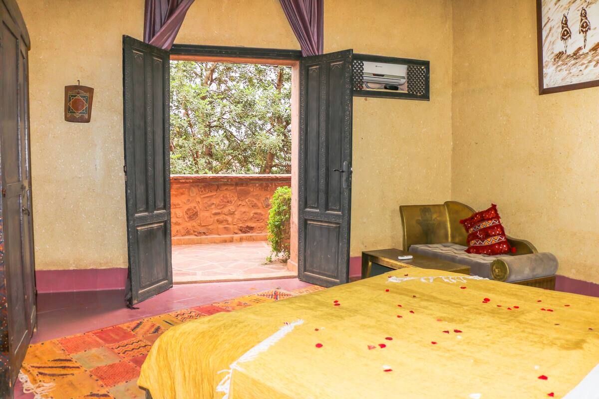 A room with a bed, a sofa, and an open door leading to an outdoor area.