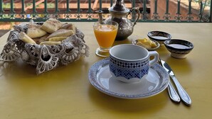 A table with a teapot, cups, and a basket of bread on a balcony overlooking a cityscape. - Kasbah Omar (Ourika)