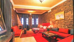 A cozy living room with a stone wall, red sofas, a fireplace, and a television. - Kasbah Omar (Ourika)