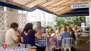 Un restaurant avec une terrasse couverte, des tables recouvertes de nappes à carreaux et un panneau indiquant l’entrée.
