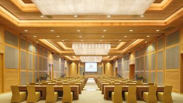 A conference room with rows of chairs, a large chandelier, and a presentation screen at the front.